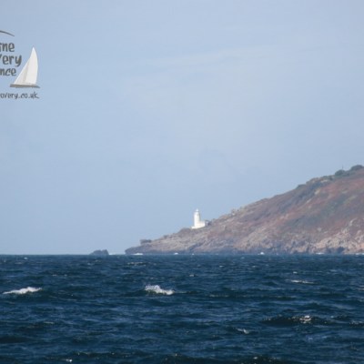 Lighthouse on a rocky coastline with choppy sea and clear sky.