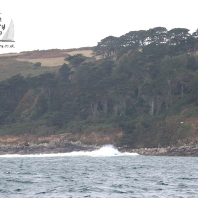 Coastal view with rocky shore, waves, and dense tree-covered hillside.