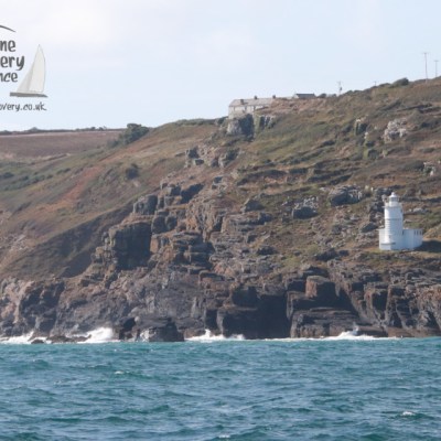 Coastal landscape with a white lighthouse on rocky cliffs under a clear sky.