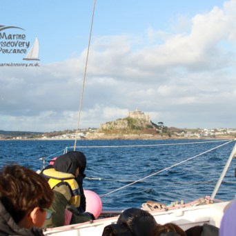 People on a boat looking at a coastal castle with sunlit clouds in the background.