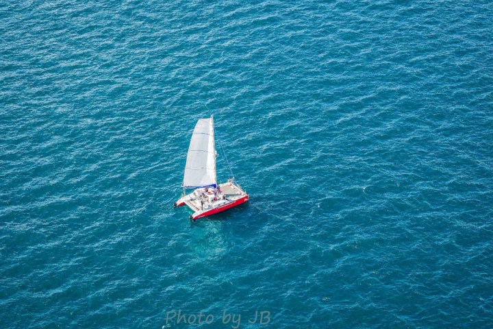 Red sailboat with white sail on vast blue ocean, aerial view.