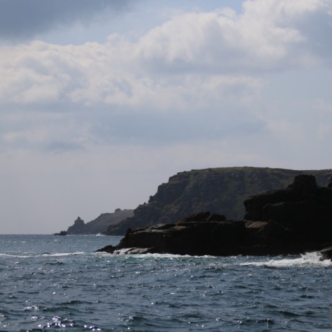 Rocky coastline with waves under a cloudy sky.