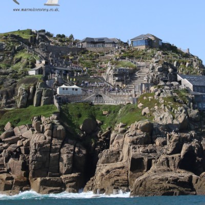 Coastal cliff with buildings and rocky terrain under a clear blue sky.