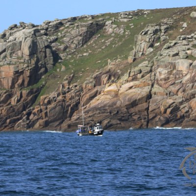 A small boat sails near a rocky cliff coastline under a clear blue sky.