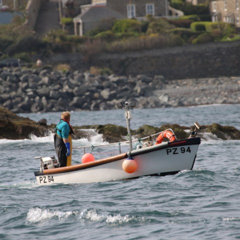 Person on small boat PZ 94 near rocky shore, cloudy sky.