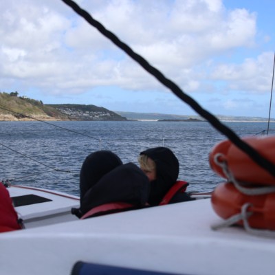People in hooded jackets on a boat with lifebuoys, overlooking a scenic coastal view.