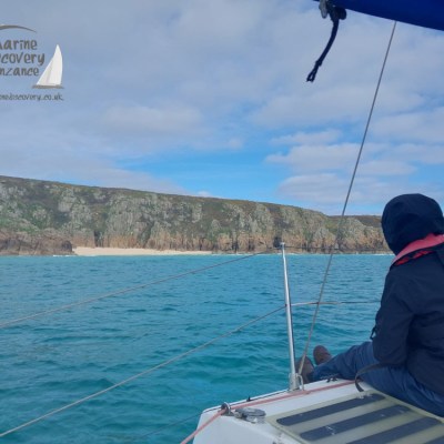 Two people on a boat looking at a rocky coastline with blue skies and clouds.