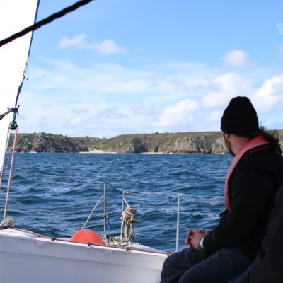 Two people on a boat looking at rocky coastline and blue sea.