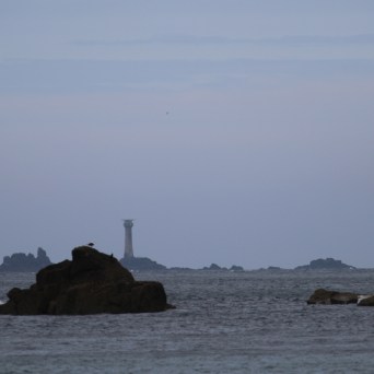Distant lighthouse on rocky islets under a cloudy sky.