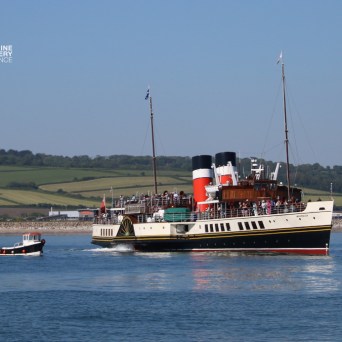 Vintage steamship and small boat on a calm sea near green hills.