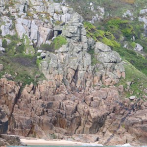 Rocky cliff with greenery above a small sandy beach and turquoise water.