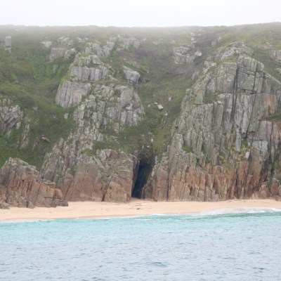 Rocky cliffs and sandy beach by the ocean under a cloudy sky.