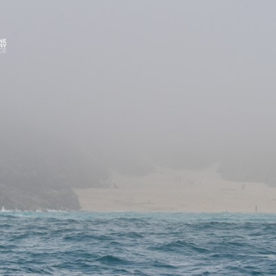 Foggy beach with rocks and turquoise sea, hazy sky.