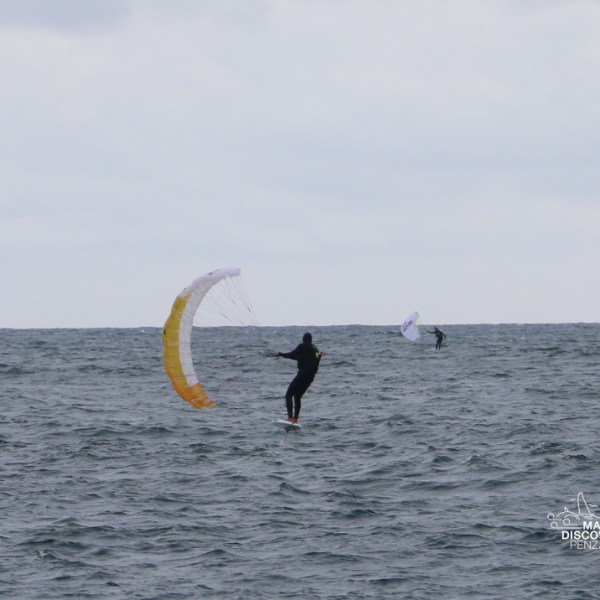 Two kiteboarders on the ocean under a cloudy sky.