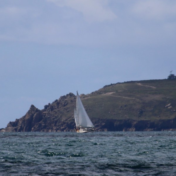 Sailboat on the sea with rocky island and cloudy sky.