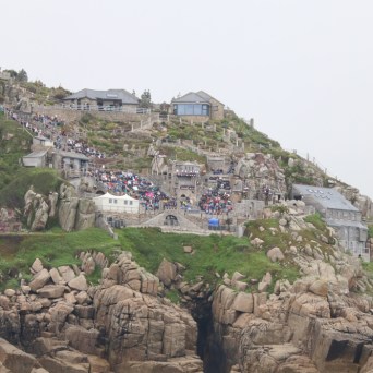 Cliffside theater and buildings with rocky coastline and ocean in foreground.