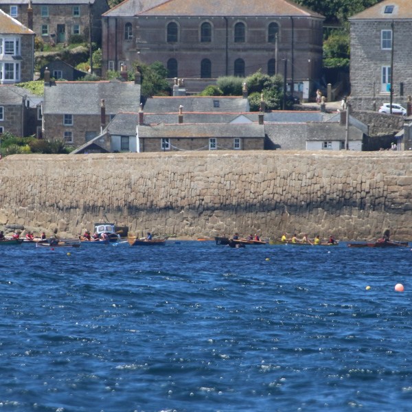Coastal houses with boats on the sea near a stone wall.