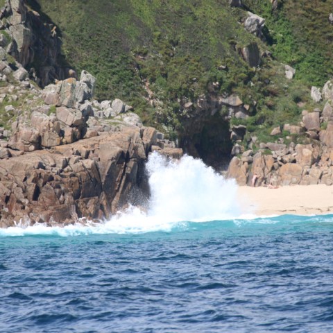 Waves crashing on rocky shore with sandy beach and lush cliffs.