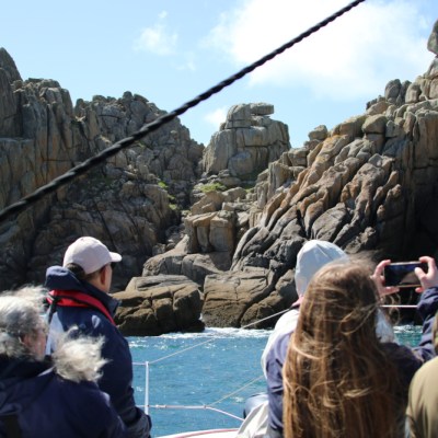 People on a boat viewing rocky cliffs under a clear sky.