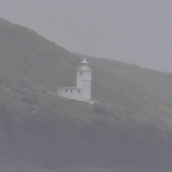 A white lighthouse on a misty, rocky coastline.