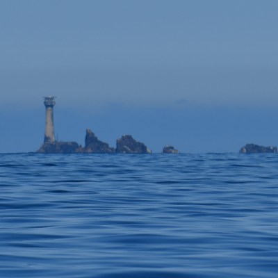 Lighthouse and rocks in calm sea under a blue sky.