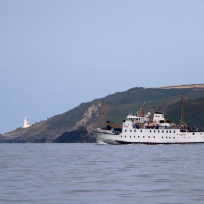 White ship sailing near a coastal hill with a lighthouse.
