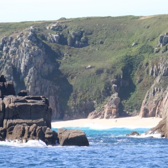 Secluded sandy beach framed by rocky cliffs and blue sea.
