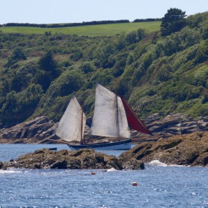 Sailboat near rocky shore with green hills in background on a sunny day.