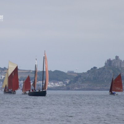 Sailboats on water with a castle on distant hill under cloudy sky.