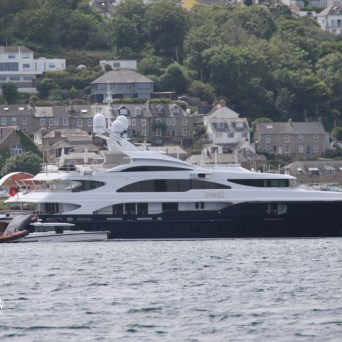 Large yacht docked near a coastal town with houses on a hill.