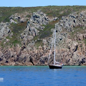 Sailboat on calm water near rocky cliffs under clear sky.