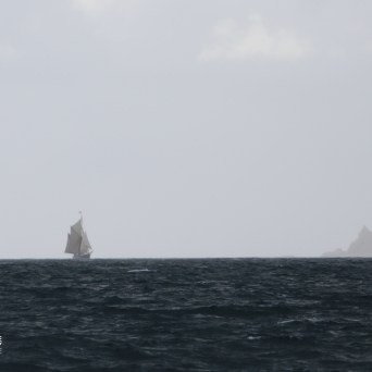 Sailing ship on misty horizon with distant land, cloudy sky.