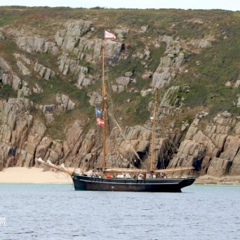 Sailing ship near rocky cliff coastline and sandy beach.
