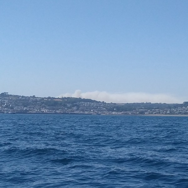 Coastal town with smoke on horizon under clear blue sky.