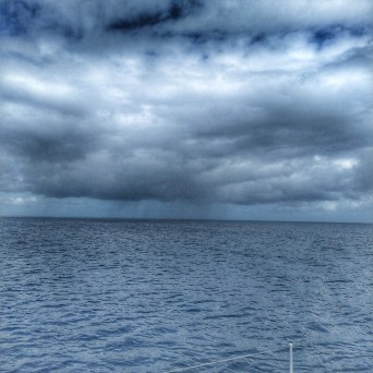 Vast ocean under a cloudy sky with rain visible on the horizon.