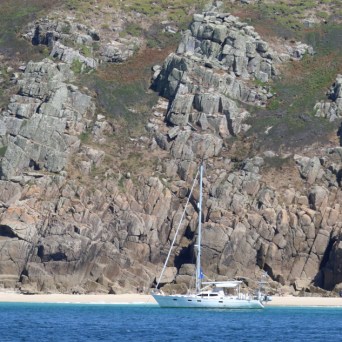 Sailboat anchored near rocky cliffs with a sandy beach.
