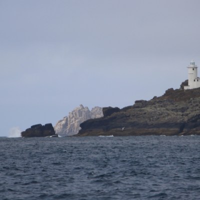 Lighthouse on rocky cliff by the sea with cloudy sky.