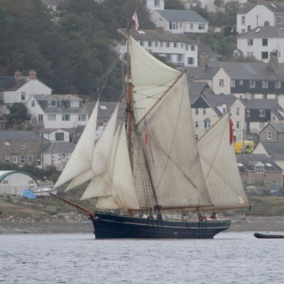 Classic sailboat with white sails near a coastal town.
