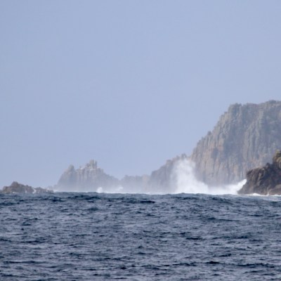 Waves crashing on rocky cliffs under a hazy sky.