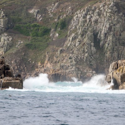 Waves crash against rugged rocky cliffs on a coastal shoreline.