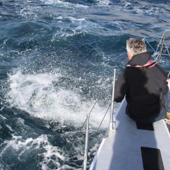 Two people on a boat looking at swirling ocean water.