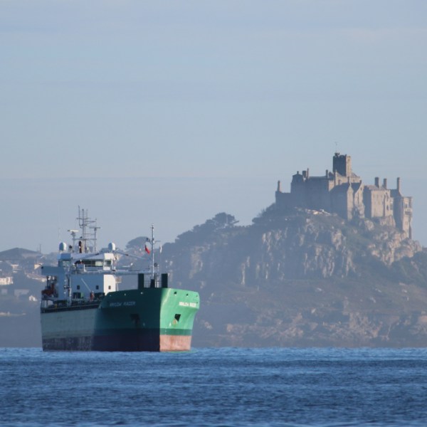 Cargo ship in water near a distant coastal castle atop a rocky hill.