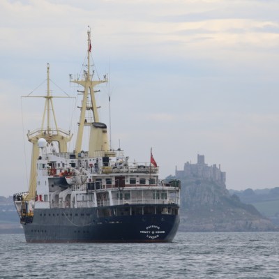 A large ship sailing near a distant castle on a cloudy day.